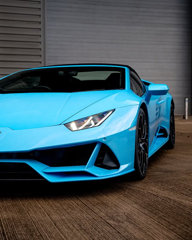 A blue sports car parked on a concrete surface next to a building with gray siding.
