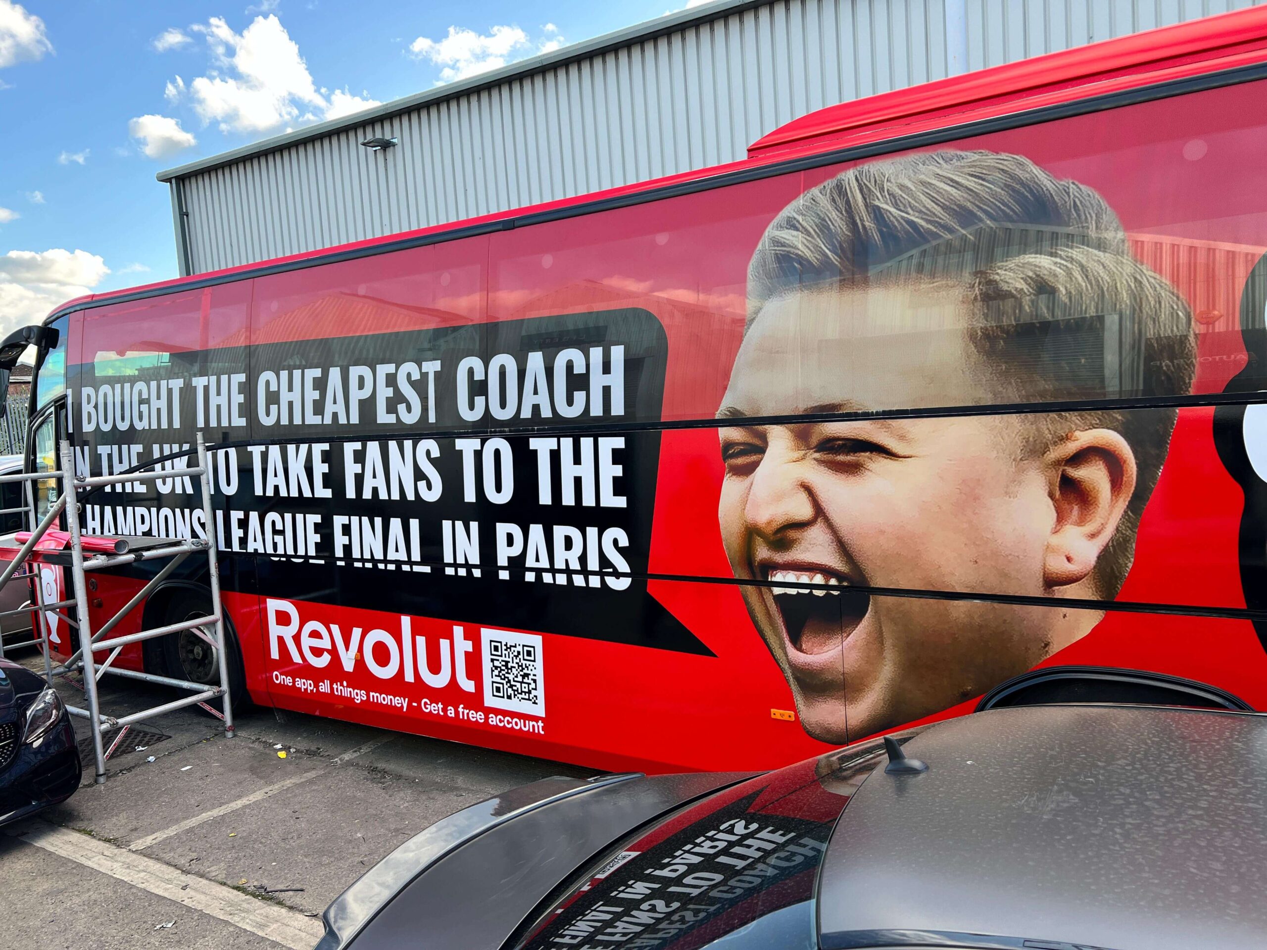 A red bus with an advertisement featuring a man's face and text about buying the cheapest coach to take fans to the Champions League Final in Paris.