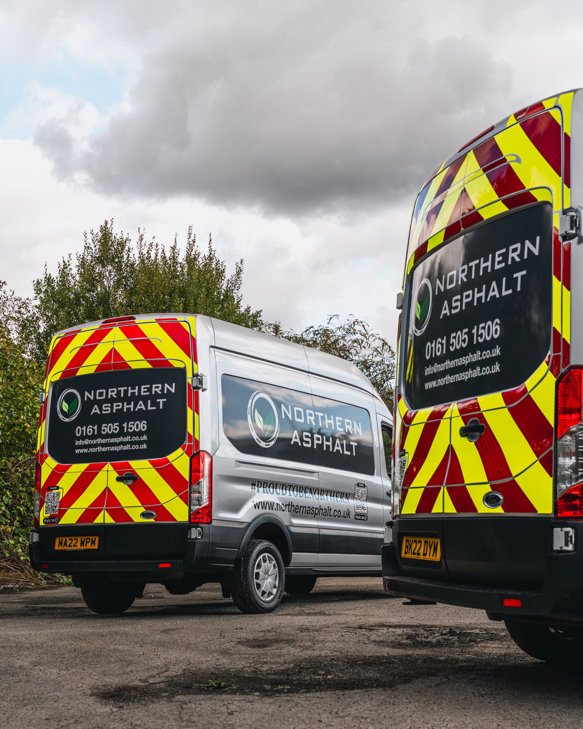 Three Northern Asphalt company vans, two with yellow and red chevron patterns on the back, are parked outdoors on an overcast day.